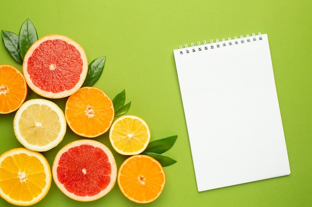 Notebook e frutas cítricas, frutas flatlay, composição mínima de verão com toranja, limão, tangerina e laranja. Cor de verão, colheita, corte de frutas
