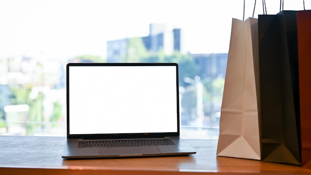 Notebook-Laptop-Mockup und Einkaufstaschen stehen auf dem Tisch vor dem Fenster-Nahaufnahmebild