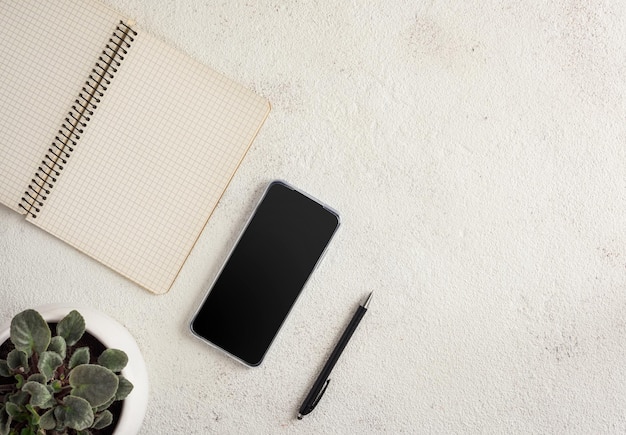 Notebook smartphone bolígrafo y maceta sobre un fondo blanco.