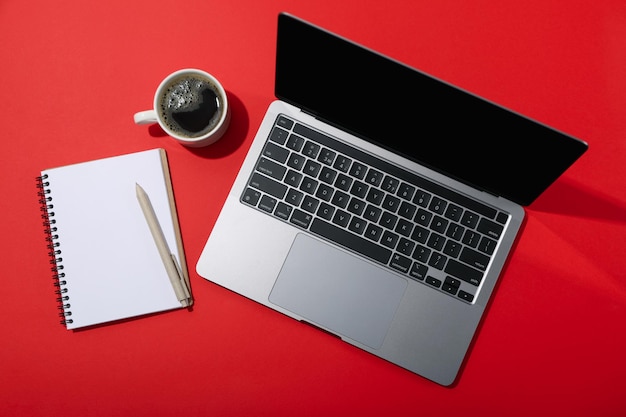 Notebook Tasse Kaffee und Laptop auf rotem Hintergrund