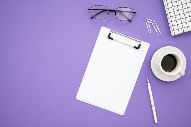 Notepad Brille Stift Kaffeetasse Büroklammern auf lila Hintergrund Flach legen