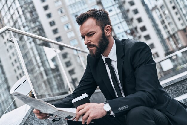 Noticias de todos los días. Apuesto joven en traje completo leyendo un periódico