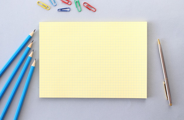 Notizblock mit Leerzeichen für Text auf einer grauen Oberfläche neben Stiften, Stift und Büroklammern.