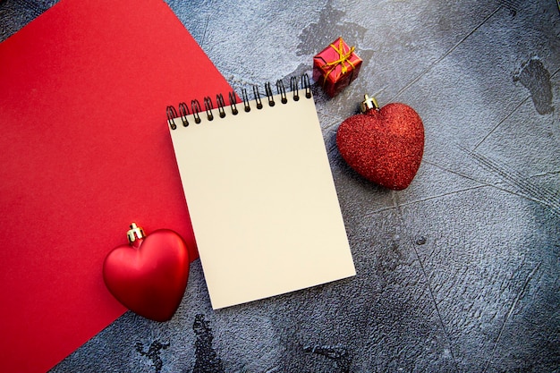 Notizblock und rote Herzen auf einem rotgrauen Hintergrund