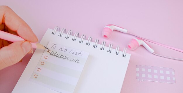 Notizblockkopfhörer und -bleistift auf einem rosa Hintergrund