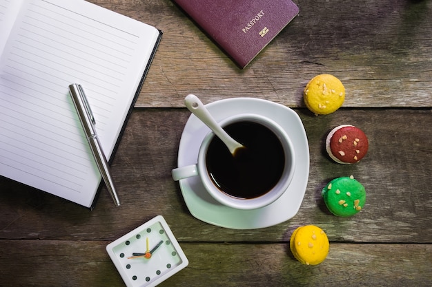 Notizbuch auf rustikalem Holz mit Makrone und Tasse Kaffee und Pass und Uhr