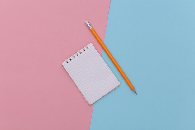 Notizbuch mit Bleistift auf einem blau-rosa Pastellhintergrund. Ansicht von oben