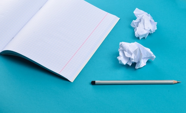 Notizbuch mit Bleistift und weißer zerknitterter Papierkugel auf blauem Hintergrund