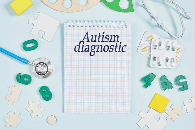 Notizbuch mit der Aufschrift Autismusdiagnostik auf blauem Hintergrund, Lernspielzeug, Medikamente, Kinderbrille und Stethoskop-Draufsicht