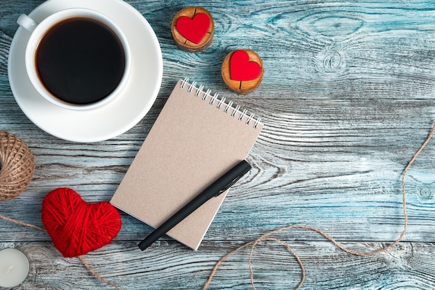 Notizbuch mit einem Stift, Kaffee und roten Herzen auf einem hölzernen Hintergrund.