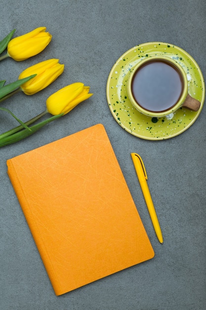 Notizbuch mit Stift und Kaffeetasse und Blumen auf grau