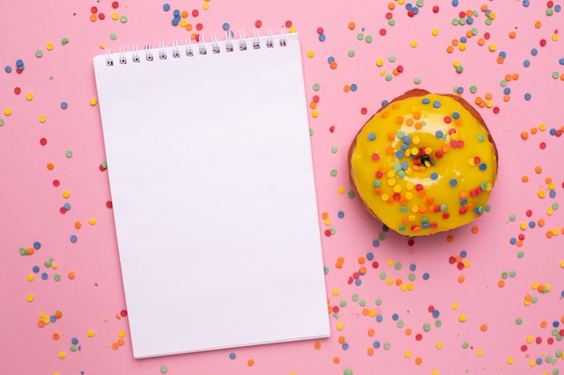 Notizbuch und gelber süßer Donut auf einer rosa Hintergrundebenenlage