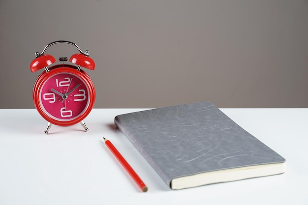 Notizbuch und rote Uhr auf dem Tisch mit Kopienraumhintergrund