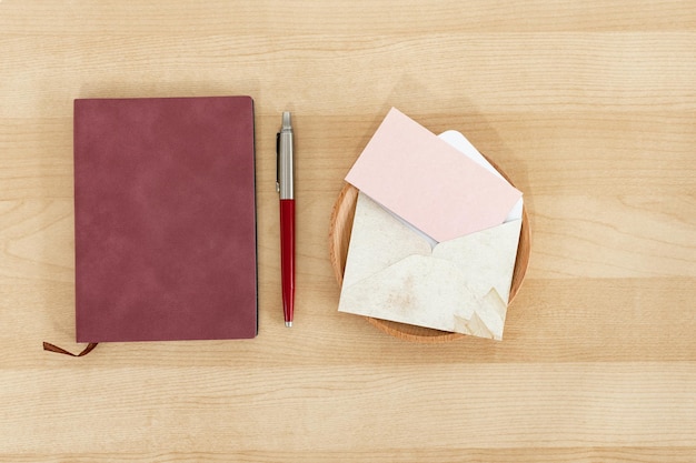 Notizbuchstift und rosa leere Papierkarte mit rustikalem Umschlag Recyclingpapier auf Holzschreibtisch