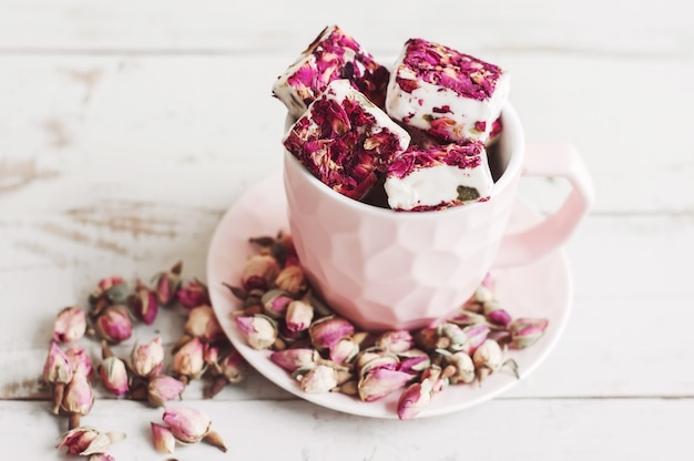 Nougat com pétalas de flores comestíveis em uma xícara de café rosa e botões de rosa secos