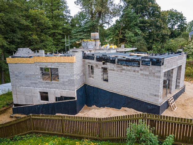 Nova casa residencial em construção com blocos de cimento e materiais de construção numa área arborizada