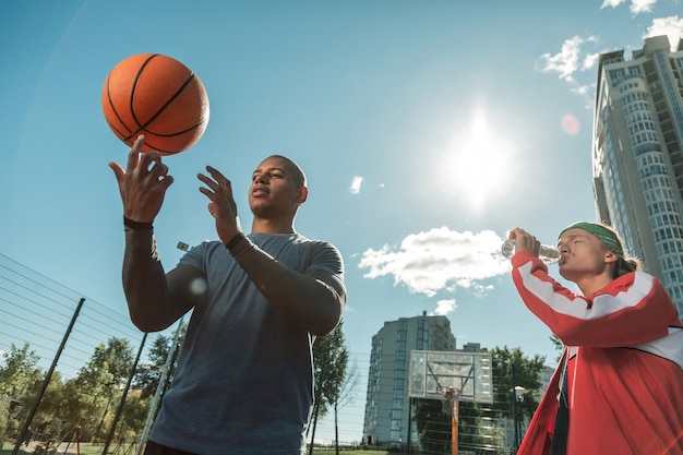 Nova habilidade. jovem simpático aprendendo a girar a bola ao lado de seu amigo