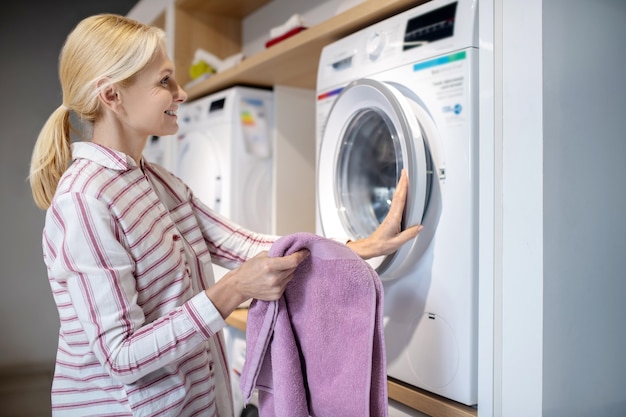 Nova máquina de lavar. mulher loira com camisa listrada em pé perto da máquina de lavar