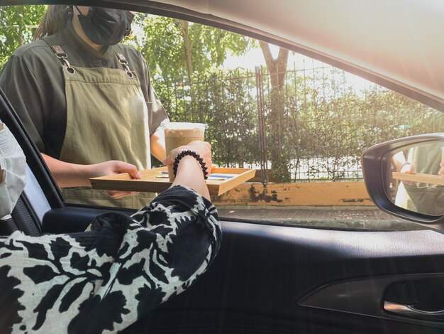 Nova mulher normal sentada em um carro e recebendo café gelado no drive through