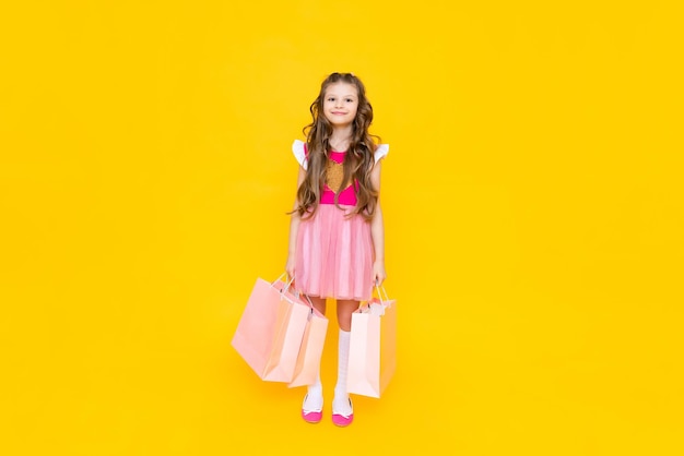 Novas compras para o verão uma garotinha volta da loja com grandes sacolas de coisas Uma criança em um vestido rosa com sacolas de compras em um fundo isolado