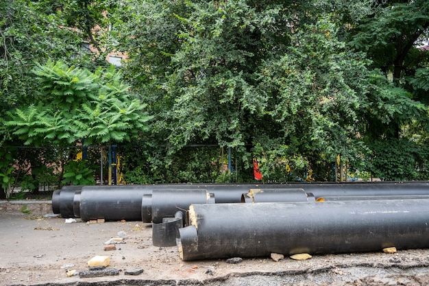 Novas tubulações de água preta isoladas ao ar livre em um dia de verão, perto de árvores verdes. Conceito de infraestrutura de esgoto urbano, modernização e reconstrução de sistema subterrâneo.