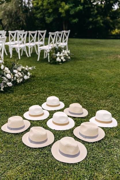 Nove chapéus de verão brancos e bege colocados na grama verde em uma festa de casamento