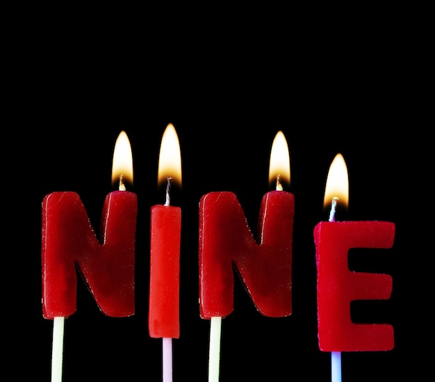 Nove soletrados em velas de aniversário vermelhas contra um fundo preto