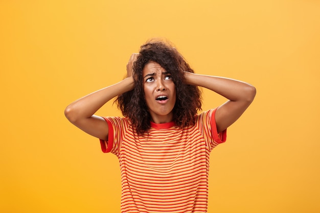 Novia africana con las manos en la cabeza y el ceño fruncido mirando insatisfecho sobre la pared naranja