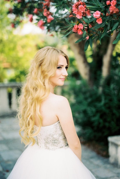 La novia se para al lado de un árbol que florece con flores rosas