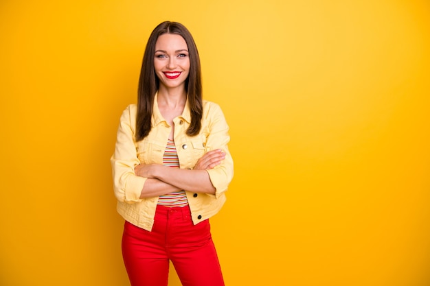 Novia alegre vistiendo pantalones rojos pantalones con los brazos cruzados en camiseta de rayas aislado pared de colores vivos