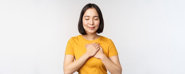 Novia asiática romántica cogidos de la mano en el corazón sonriendo con cuidado y ternura de pie en camiseta amarilla sobre fondo blanco.