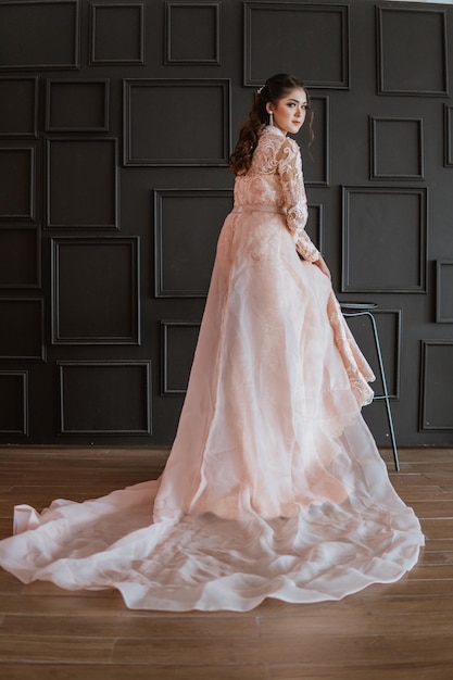 Novia asiática con vestido naranja de cola larga de pie y mirando hacia atrás en el estudio fotográfico