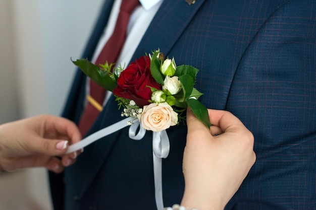 La novia ata una flor en el ojal al novio en la chaqueta