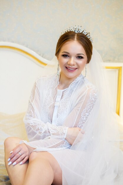 La novia con una bata blanca en la cama en una mañana de bodas