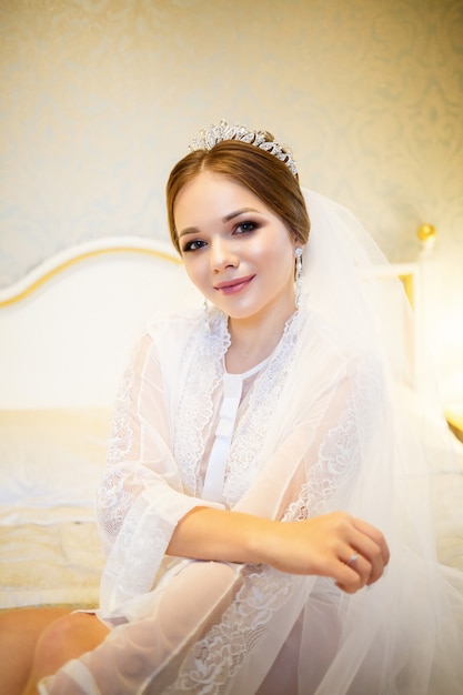 La novia con una bata blanca en la cama en una mañana de bodas