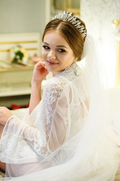 La novia con una bata blanca en la cama en una mañana de bodas