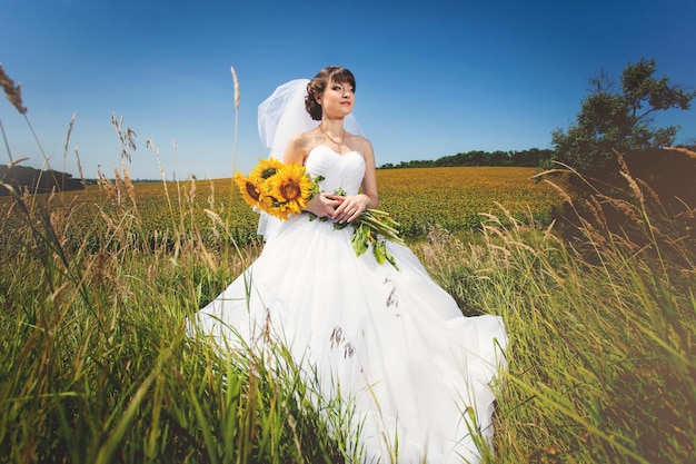 Novia de belleza en campo con ramo de girasoles