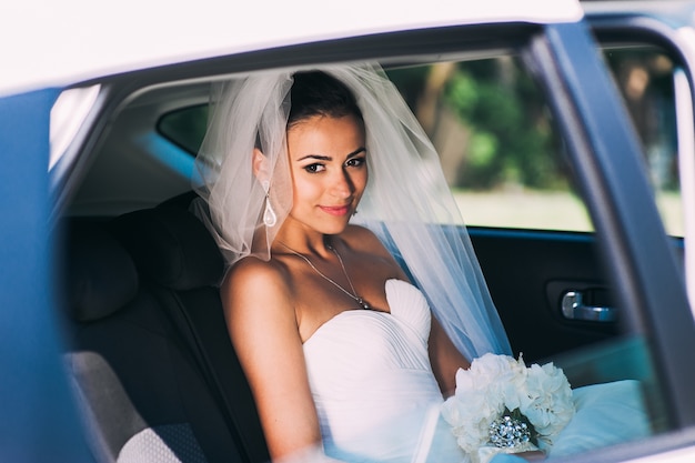 Novia de belleza en vestido de novia con velo de encaje en el coche