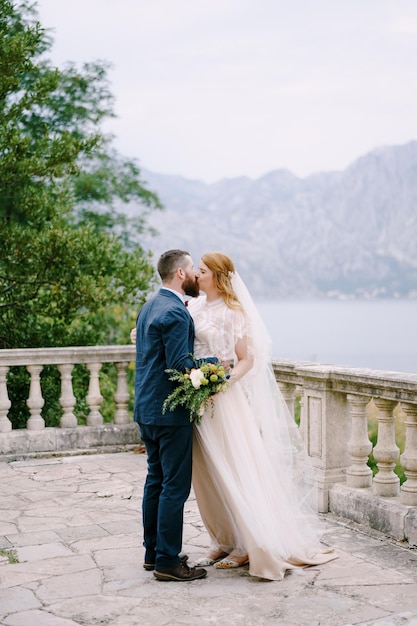 La novia besa al novio en la terraza de piedra con el fondo del mar