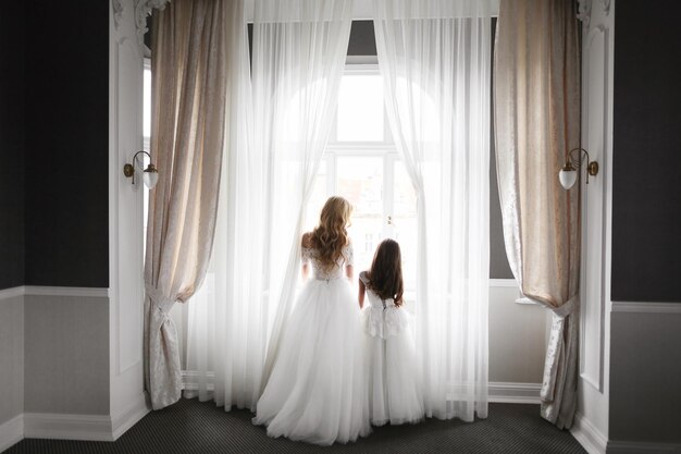 Novia de la boda en un hermoso vestido sentado en un sofá en el interior de un estudio blanco como en casa Estilo de boda de moda filmado en toda su longitud Joven modelo morena caucásica atractiva como una novia