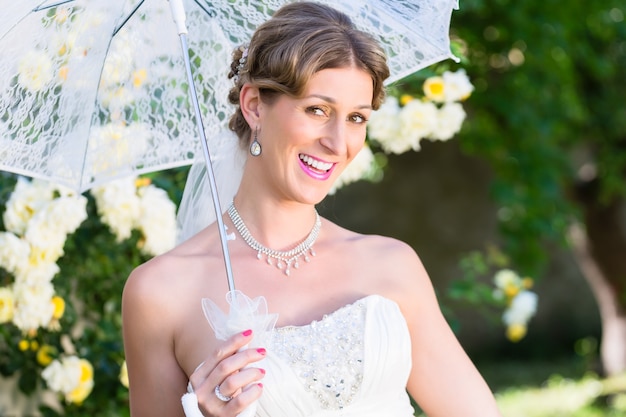 Novia en boda con sombrilla en el jardín de verano