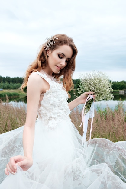 Novia bonita joven en vestido de novia blanco al aire libre