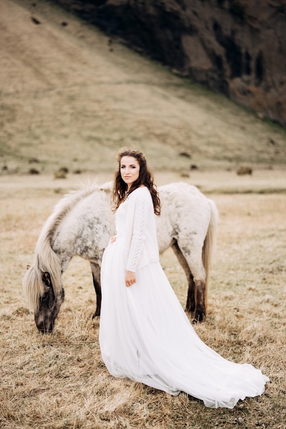 Novia camina por el campo junto a un caballo blanco