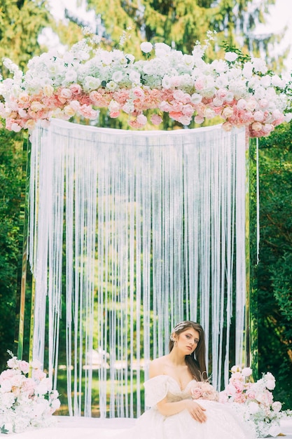 Novia cerca del arco de boda con flores.