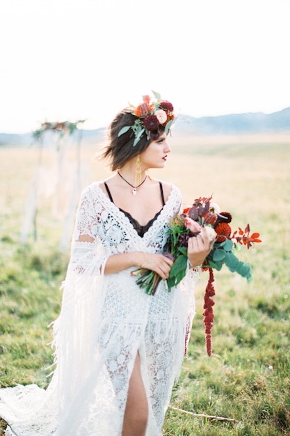 La novia en una corona con un ramo de flores se encuentra en un campo con la cabeza vuelta hacia un lado