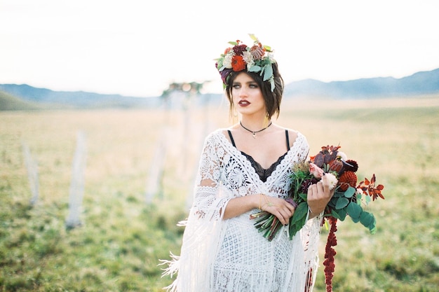 Novia en una corona con un ramo de flores se encuentra en un campo