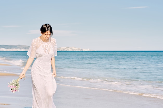 Novia corriendo felizmente por la playa con su vestido de novia y sosteniendo un ramo de flores en la mano