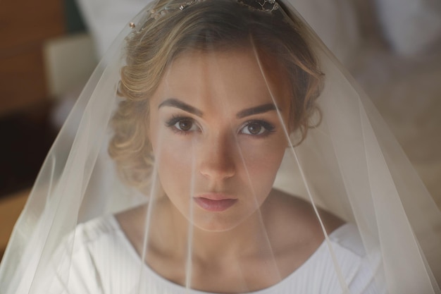 La novia cubierta con un velo se sienta en una silla en el hotel.