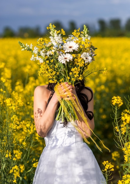 La novia se cubrió la cara con un ramo de novia con flores amarillas Una mujer en un campo de colza