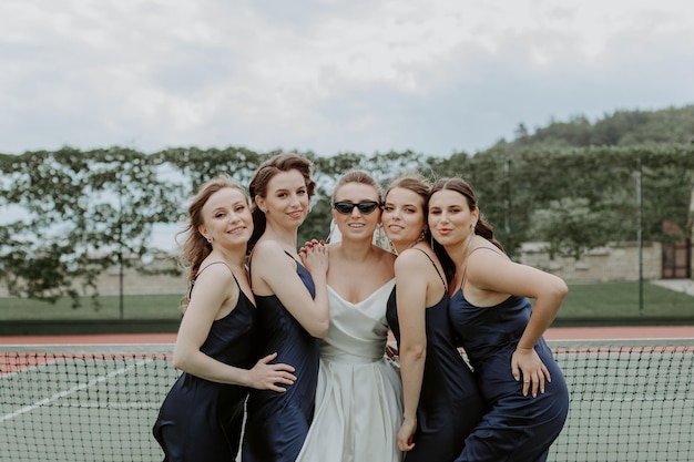 Novia con las damas de honor en los vestidos brillantes en la cancha de tenis